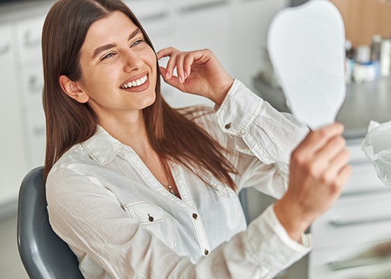 A smiling woman sitting in a dentist’s chair and admiring her pretty teeth