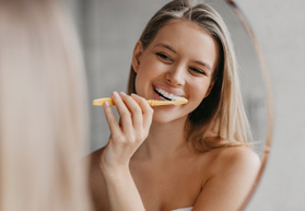 Woman brushing her teeth and smiling in the mirror