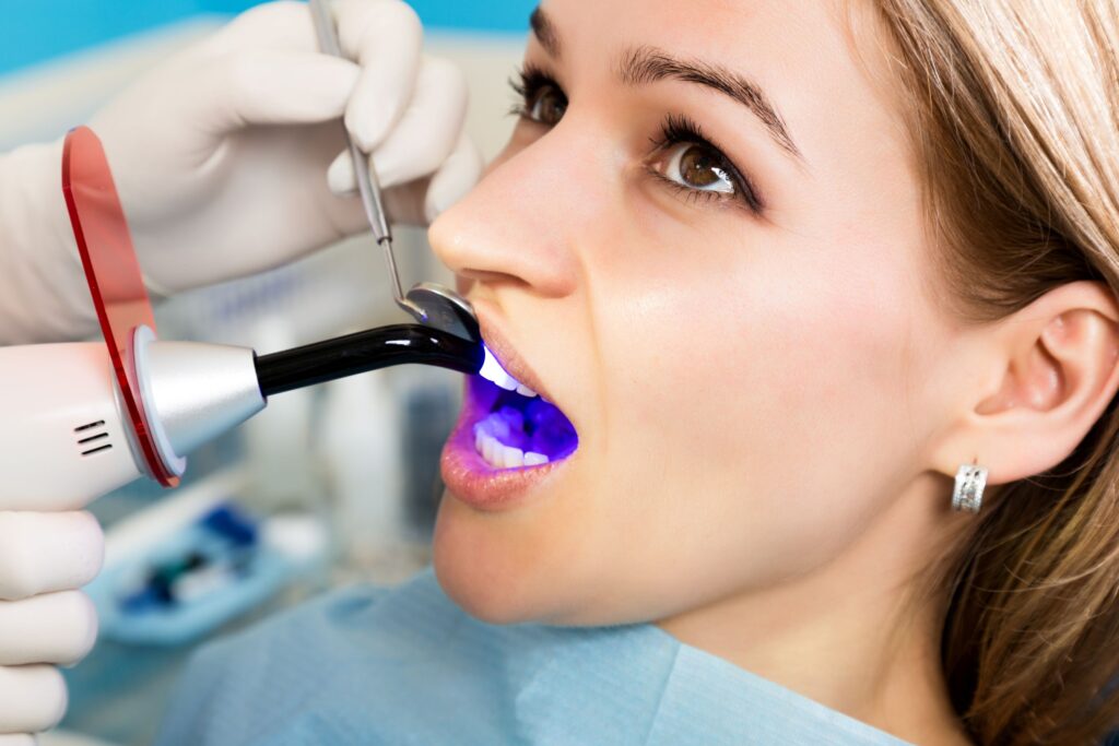 Dentist curing woman's dental bonding with ultraviolet light